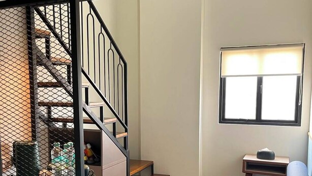 A compact living space with a staircase, a sofa, a small table, and a window. - Du Palais Hotel (Jambi)