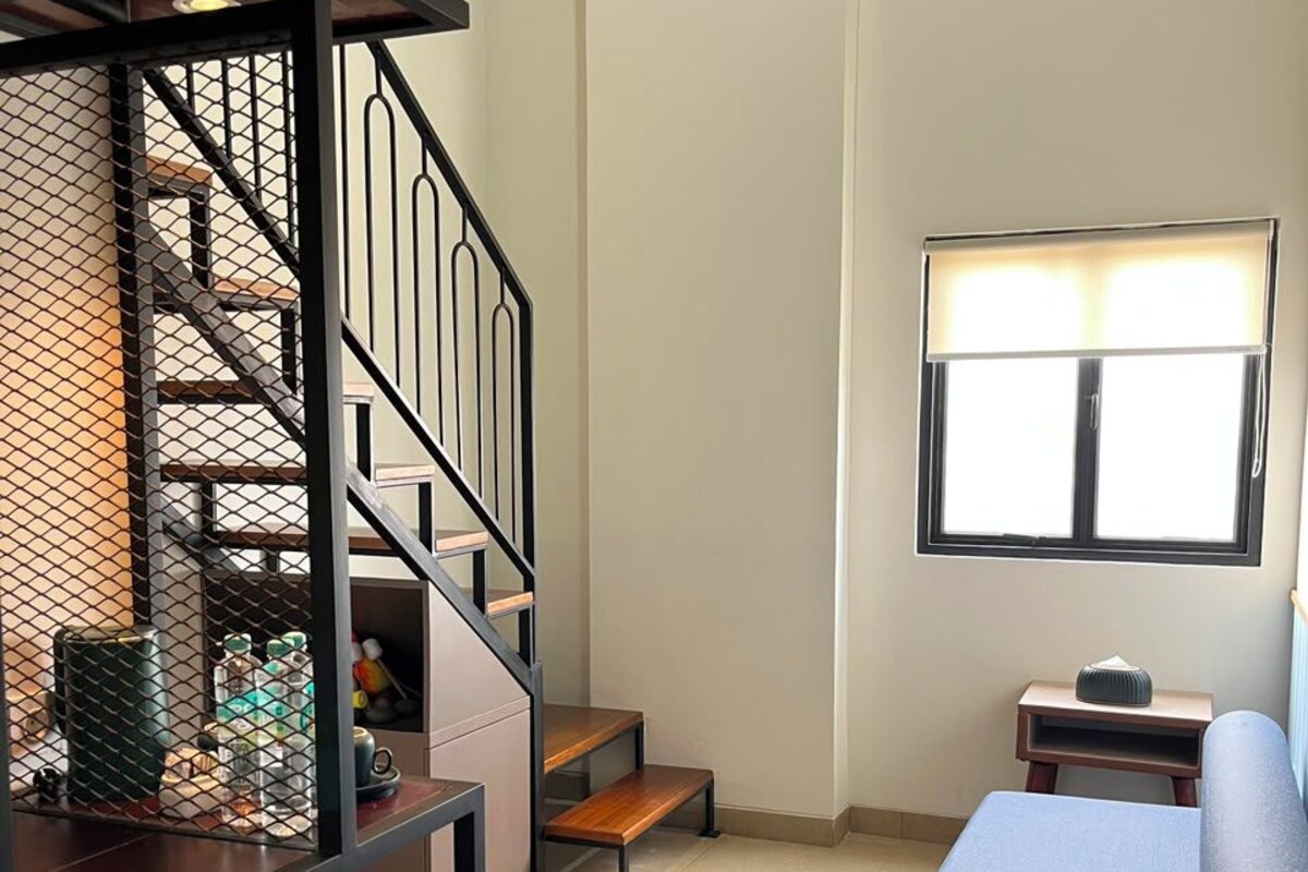 A compact living space with a staircase, a sofa, a small table, and a window.