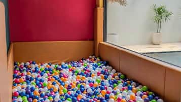 Ein Zimmer mit einem bunten Ballbecken, einer roten Wand und einem Fenster mit Blick auf eine Pflanze draußen.
