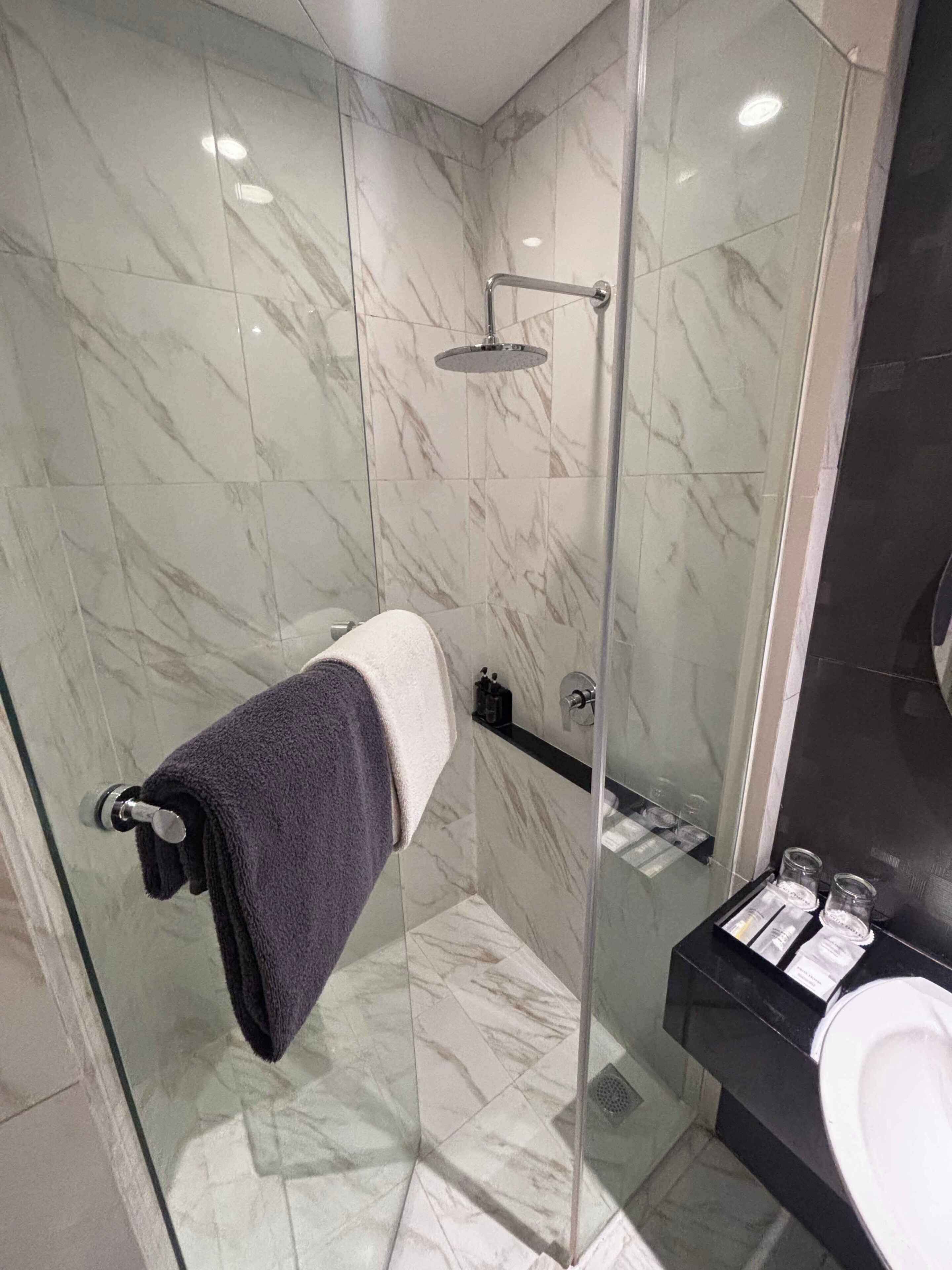A modern bathroom with a glass shower enclosure, marble tiles, a towel rack with a towel, and a sink with toiletries.