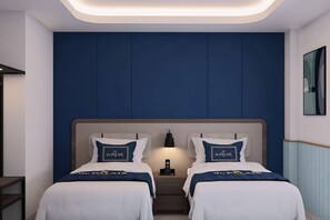 Habitación de hotel con dos camas, una mesita de noche, una lámpara y un cuadro en la pared.