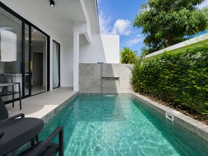 Ein moderner Poolbereich im Freien mit einem klaren, blauen Pool, einer Sitzgelegenheit mit Stühlen und einer Glastür, die zu einem Raum führt.