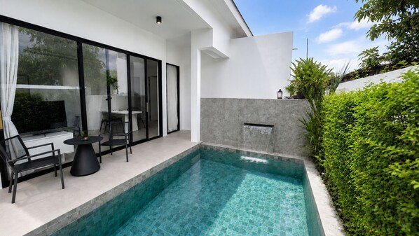 A modern outdoor pool with a glass enclosure, a seating area with chairs and a table, and a waterfall feature. - Villa Luna 2BR Private Plunge Pool (Si Sunthon)