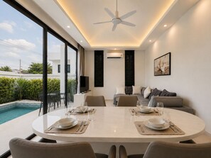 Ein moderner Essbereich mit Blick auf einen Pool, inklusive Deckenventilator und einer gepolsterten Couch.