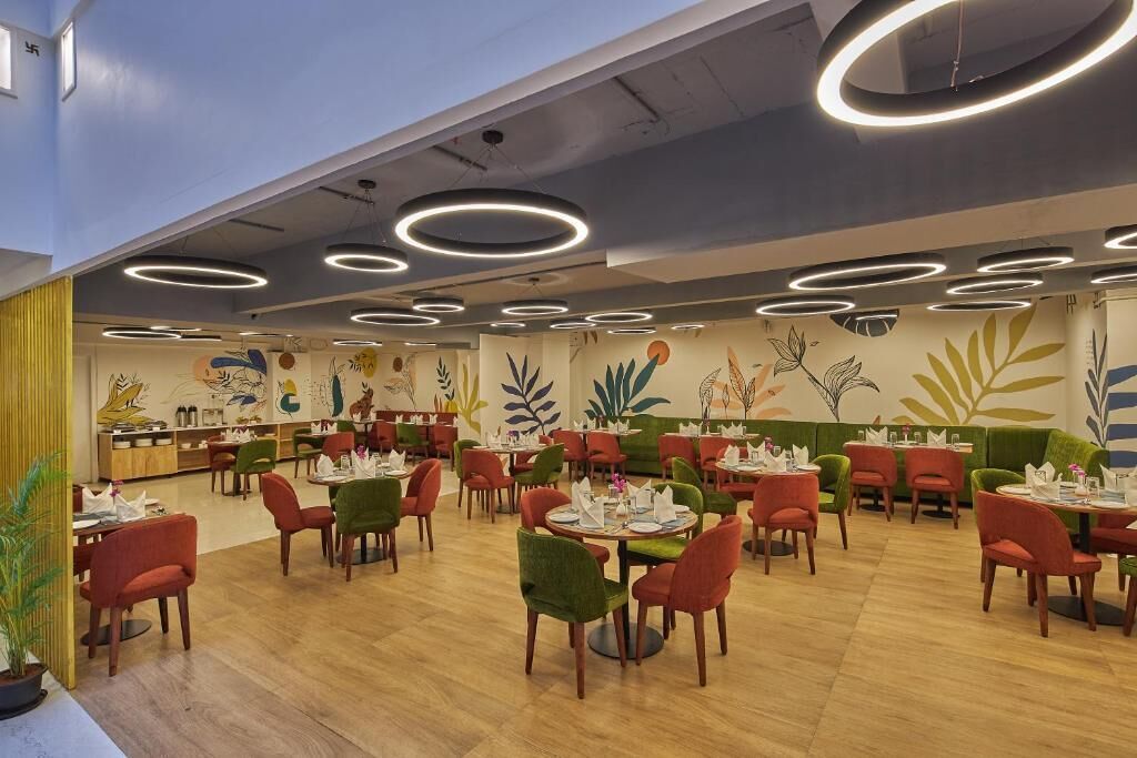 A restaurant with round tables and chairs, a ceiling with circular light fixtures, and a mural with plant designs on the wall.