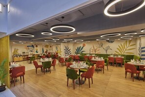 Un restaurante con mesas y sillas redondas, un techo con luminarias circulares y un mural con motivos vegetales en la pared.