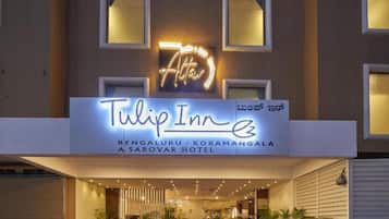 The exterior of Tulip Inn, featuring a neon sign, a modern entrance with potted plants, and a well-lit facade.