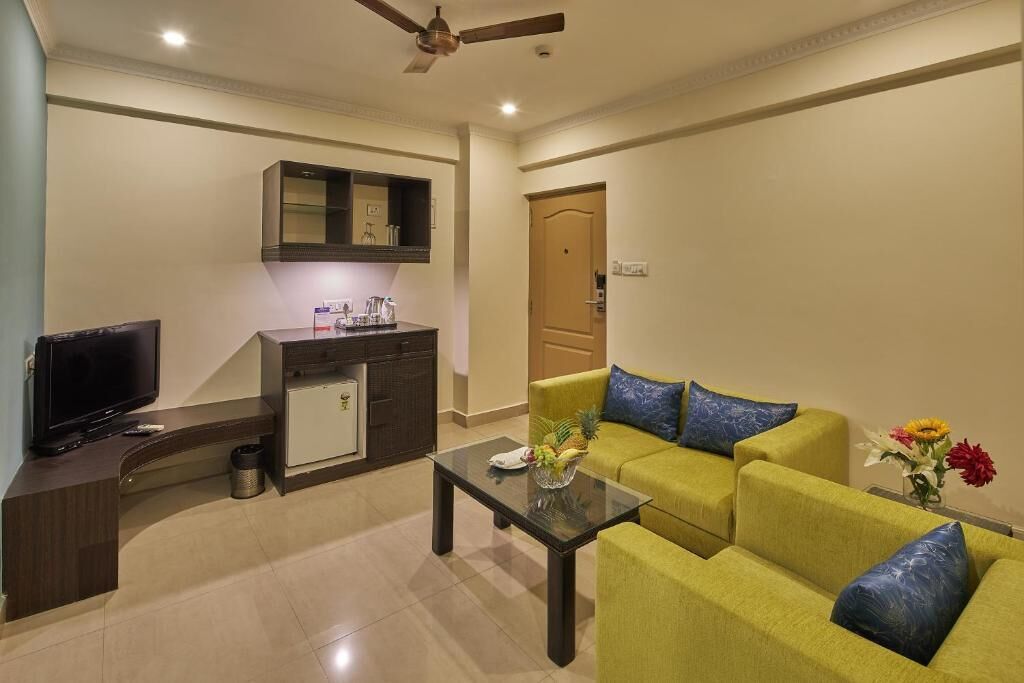A living room with a sofa, a coffee table, a TV, a kitchen area, and a ceiling fan.