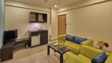 A living room with a sofa, a coffee table, a TV, a kitchen area, and a ceiling fan.