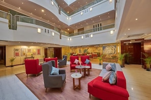 Een hotellobby met meerdere niveaus, rode en grijze zitplaatsen, een centraal eetgedeelte en een groot bord met de tekst 'Alar'