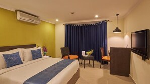 Quarto de hotel com uma cama, duas cadeiras, uma mesa pequena, uma televisão e um ar condicionado.