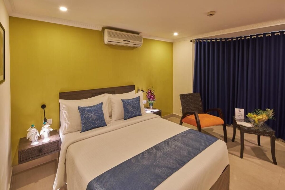 Een hotelkamer met een bed, een stoel, een tafeltje, een airconditioner en een gordijn.