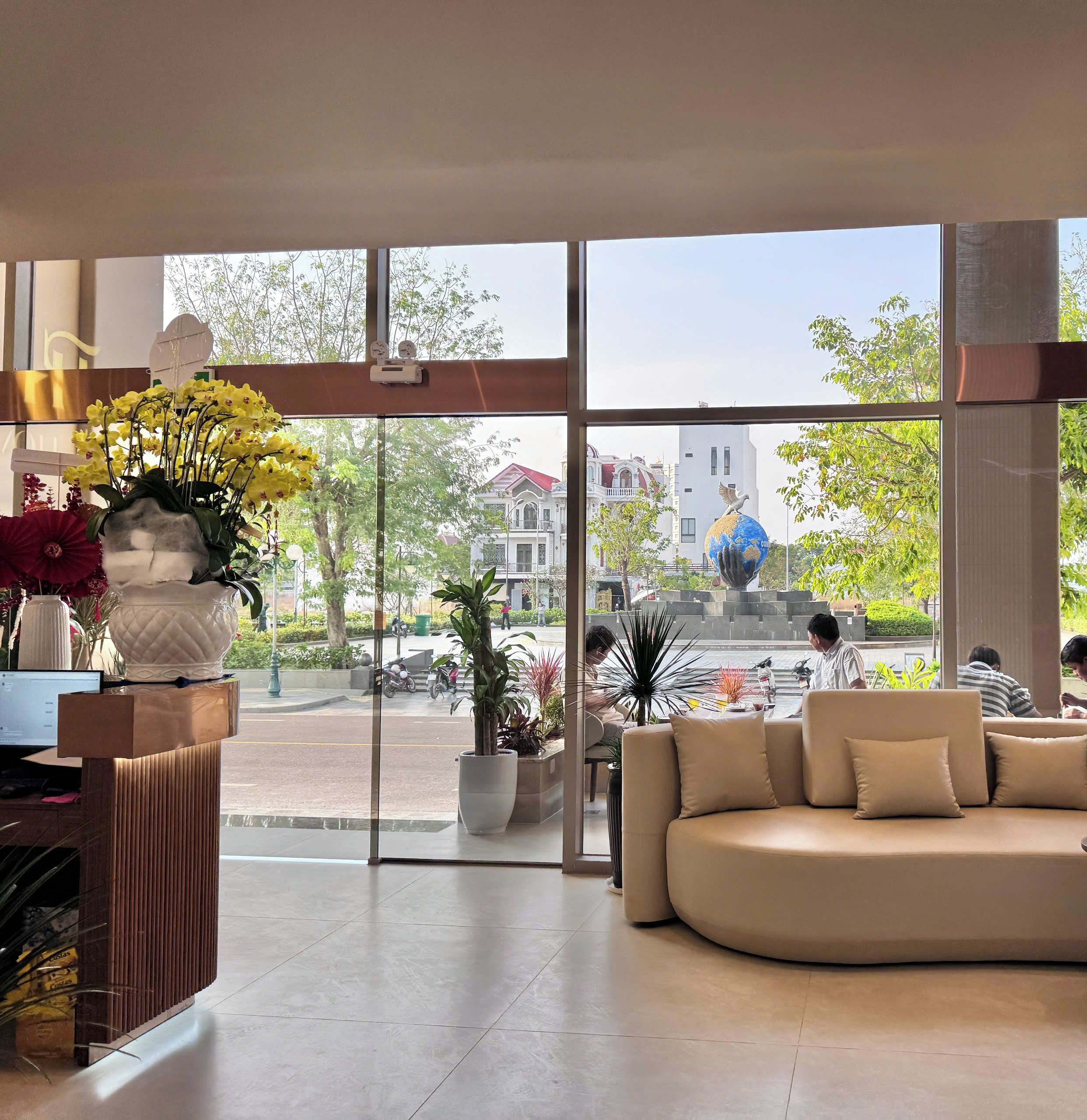 A modern interior with large windows, a sofa, a desk with a computer, and potted plants.