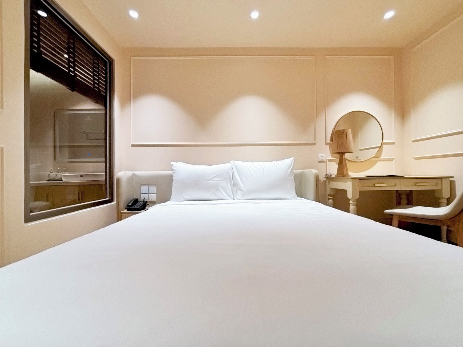 Ein Hotelzimmer mit einem großen Bett, einem Nachttisch mit Lampe, einem Schreibtisch mit Stuhl und einem Spiegel.