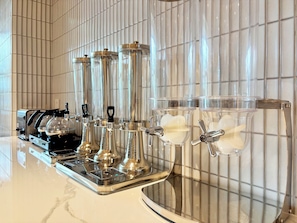 A kitchen with a coffee machine, four stainless steel dispensers, and a glass container with a white substance. - Peace Home Boutique Hotel Phan Thit (Phan Thiet)