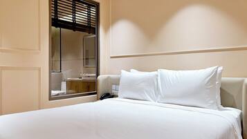 A hotel room with a bed, a bedside telephone, and a window with blinds.