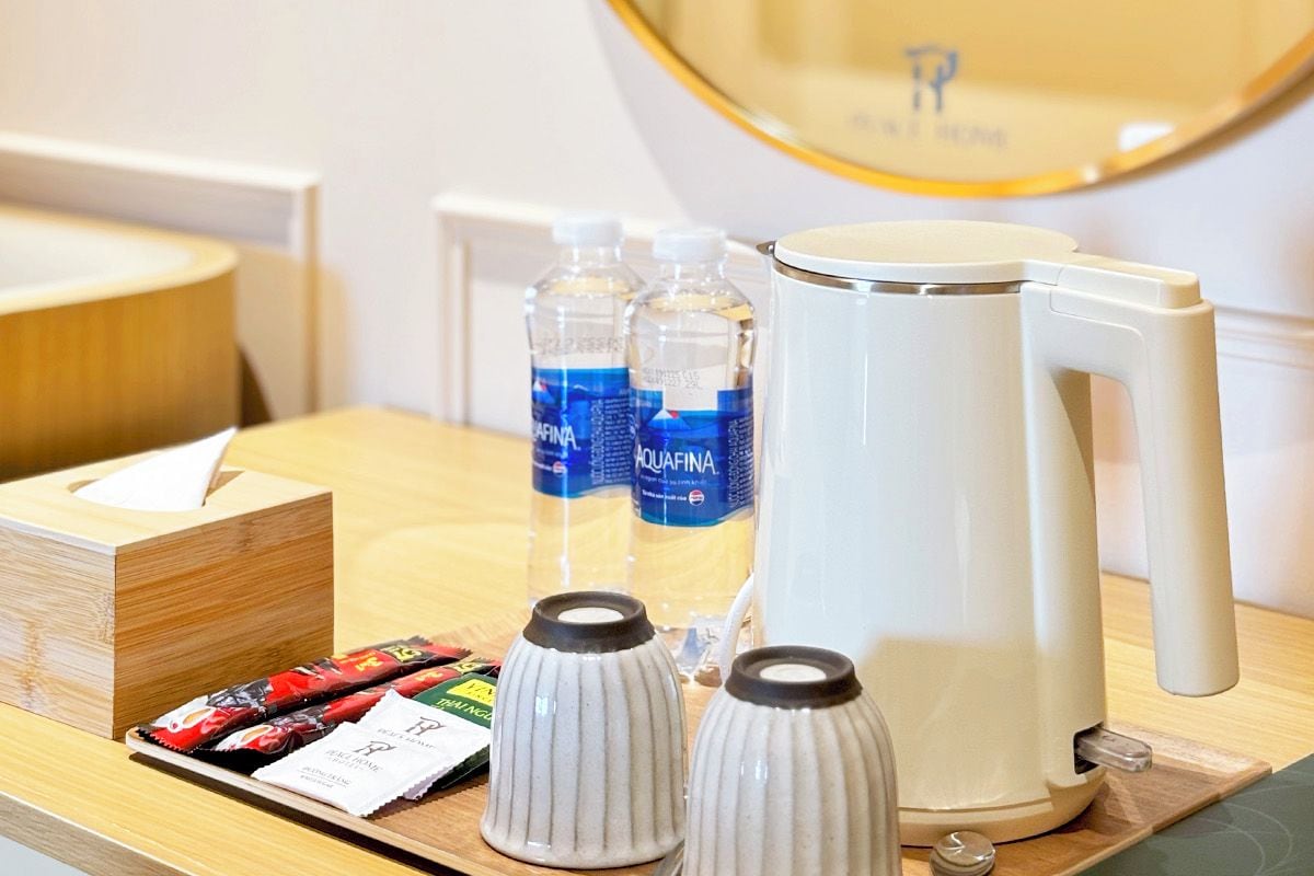 Habitación de hotel con escritorio de madera, espejo, televisor, agua embotellada, cafetera y caja de pañuelos.