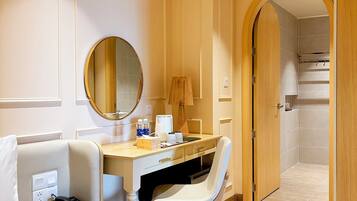 A hotel room with a bed, a desk, a chair, a mirror, a lamp, and a shower area.