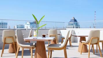Eine Dachterrasse mit Tischen und Stühlen, einem Blumentopf und Blick auf eine Stadtansicht.