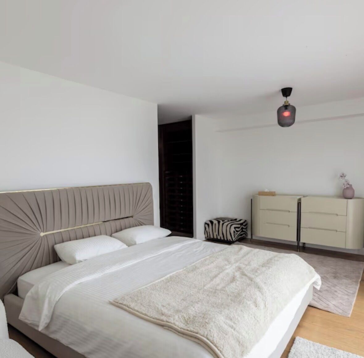 Ein modernes Schlafzimmer mit Bett, Kommode und Deckenleuchte.