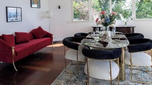A dining area with a round table, chairs, and a chandelier. There is a red sofa and artwork on the walls. - Elite Villa Geneva (Cologny)