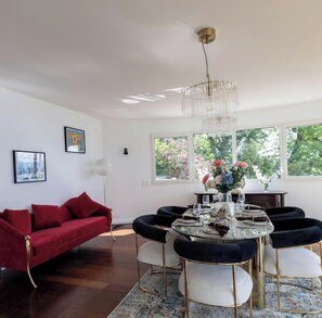 Ein Essbereich mit einem runden Tisch, Stühlen und einer Kronleuchter. Ein rotes Sofa und Kunstwerke sind an den Wänden zu sehen.