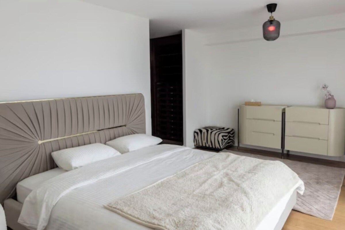 A modern bedroom with a bed, a dresser, and a ceiling light.