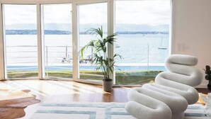 A spacious room with large windows offering a view of the sea and boats, a modern spiral chair, and a potted plant.