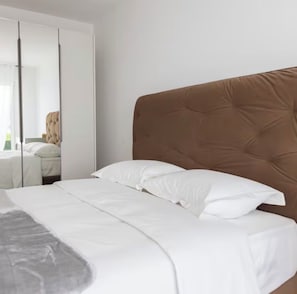 Ein Schlafzimmer mit einem Bett, weißer Bettwäsche, einem braunen Kopfteil und einem Spiegel.