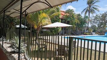 Área externa coberta com piscina, palmeiras e espreguiçadeiras.