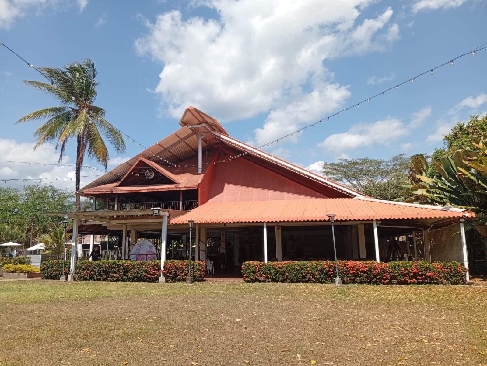 A building with a red roof, a covered porch, and a garden with red flowers.