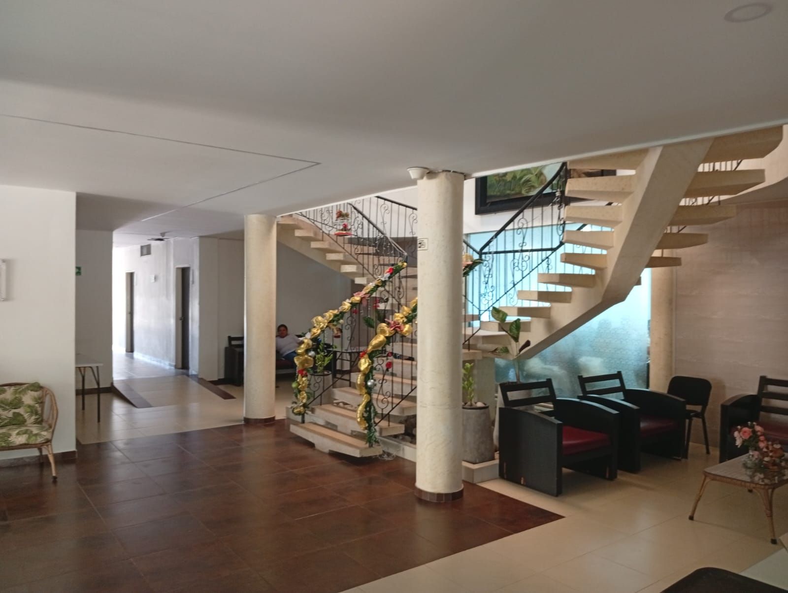 Um hall amplo com uma escadaria central, uma área de estar com cadeiras e um arranjo de plantas decorativo.