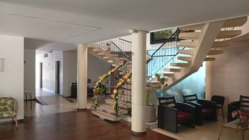Um hall amplo com uma escadaria central, uma área de estar com cadeiras e um arranjo de plantas decorativo.