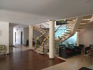 Een ruime lobby met een centrale trap, een zithoek met stoelen en een decoratieve plantenstelling.