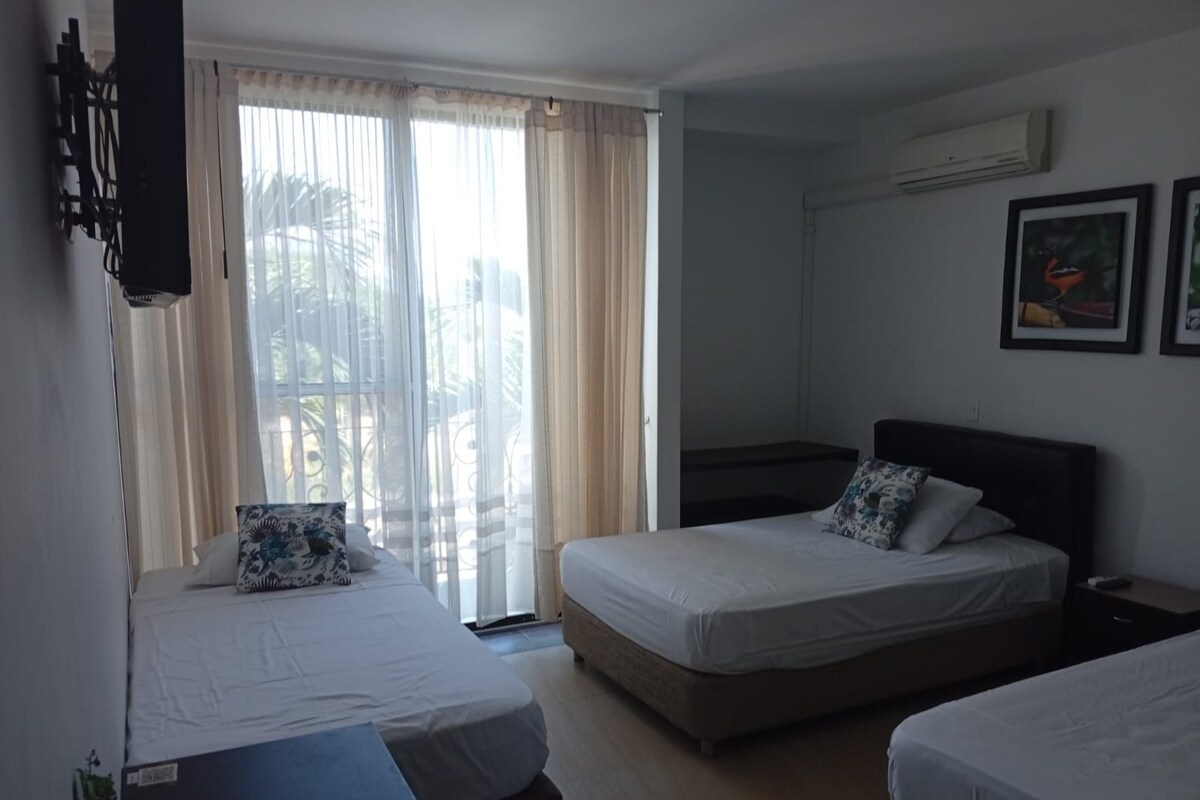Habitación de hotel con dos camas, un ventanal con cortinas, un equipo de aire acondicionado y un cuadro en la pared.