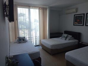 Een hotelkamer met twee bedden, een groot raam met gordijnen, een airconditioner en een lijst met een foto aan de muur.