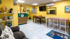 Ein Zimmer mit einer Couch, einem Esstisch mit Stühlen, einer kleinen Küchenzeile und einem an der Wand montierten Fernseher.