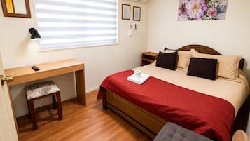 Un dormitorio con cama de madera, un escritorio, una silla, una mesita de noche y una ventana con persianas.