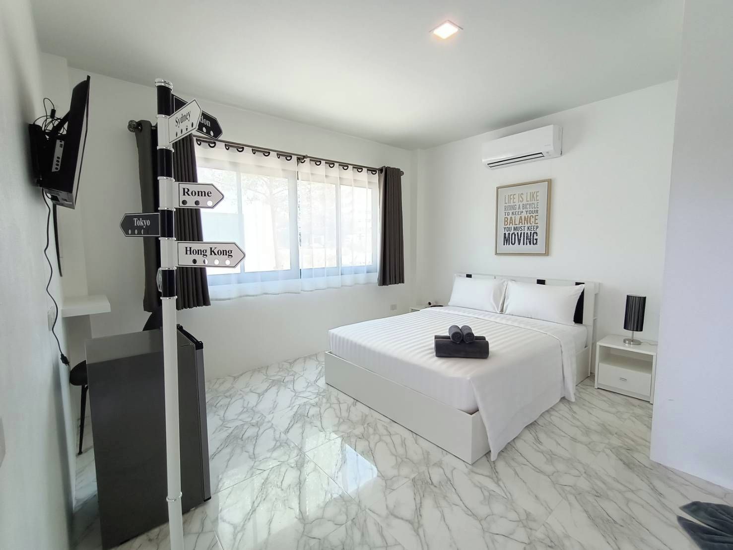 A hotel room with a bed, a desk, a TV, and a signpost with city names.