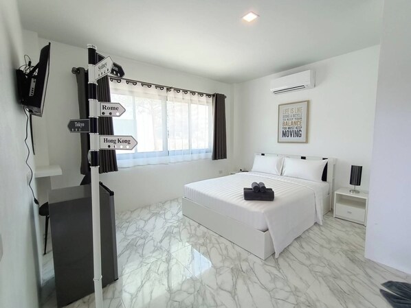 A hotel room with a bed, a desk, a TV, and a signpost with city names. - Z-beach Resort (Pranburi)