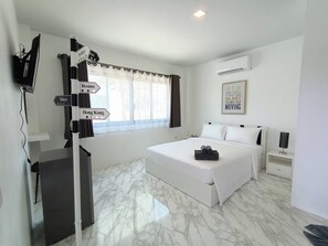 A hotel room with a bed, a desk, a TV, and a signpost with city names. - Z-beach Resort (Pranburi)