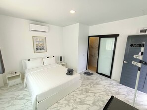 A hotel room with a bed, a nightstand, an air conditioning unit, a wall-mounted sign, a sliding door, and a directional signpost.