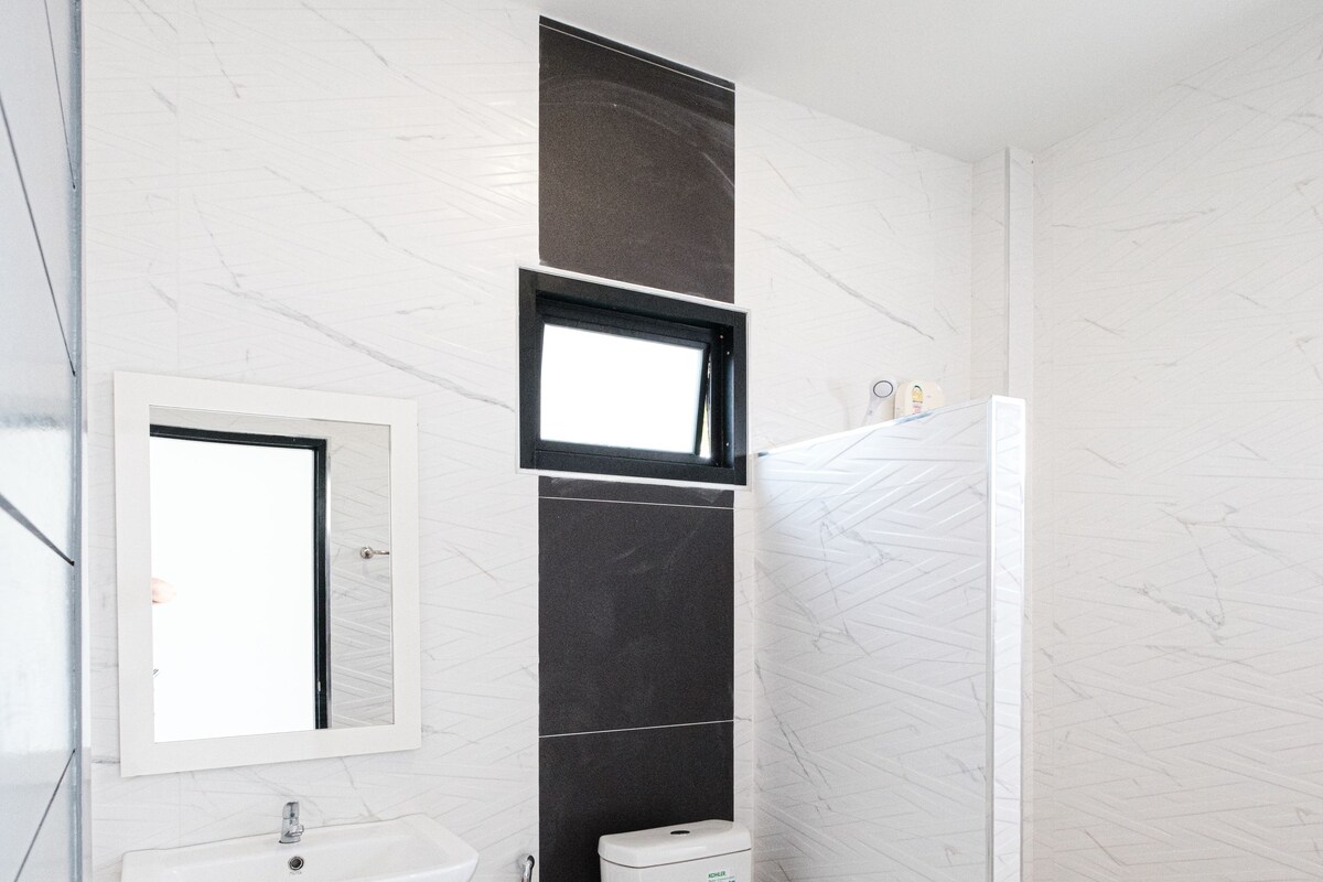 A modern bathroom with a white sink, mirror, toilet, and shower.