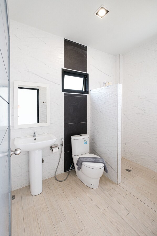 A modern bathroom with a white sink, mirror, toilet, and shower.