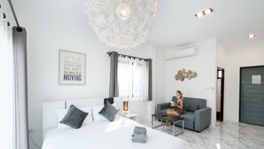 A modern hotel room with a large bed, a sitting area with a sofa and a coffee table, a decorative ceiling light, and a motivational quote on the wall. - Z-beach Resort (Pranburi)