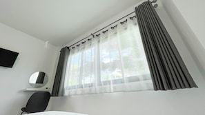 Una habitació amb un llit, un escriptori, una cadira, una finestra amb cortines i un mirall a la paret.