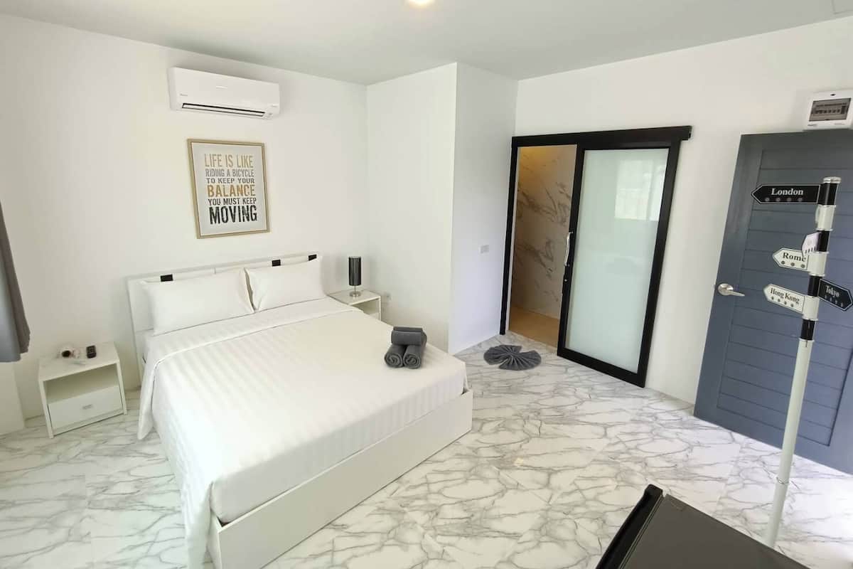 A hotel room with a bed, a nightstand, an air conditioning unit, a wall-mounted sign, a sliding door, and a directional signpost.