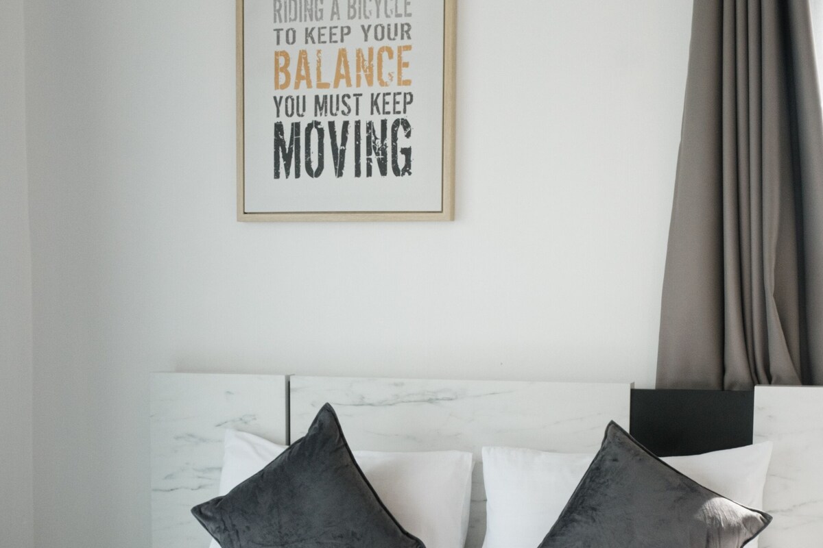 A neatly made bed with a framed inspirational quote, two pillows, and a folded towel on a white bedspread.