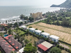 An aerial view of a coastal area with buildings, a beach, and a hilly landscape.