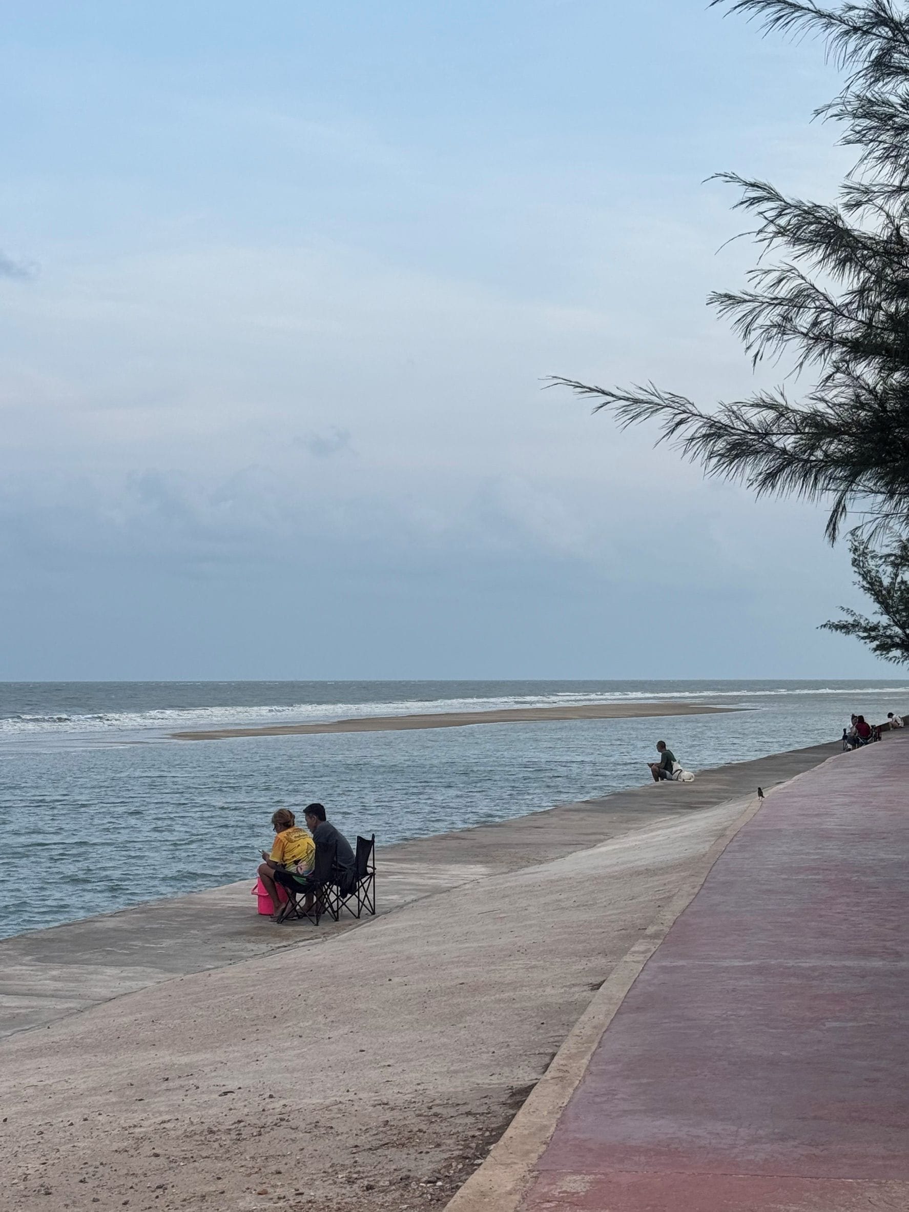 A beach with people sitting on chairs and a concrete walkway.